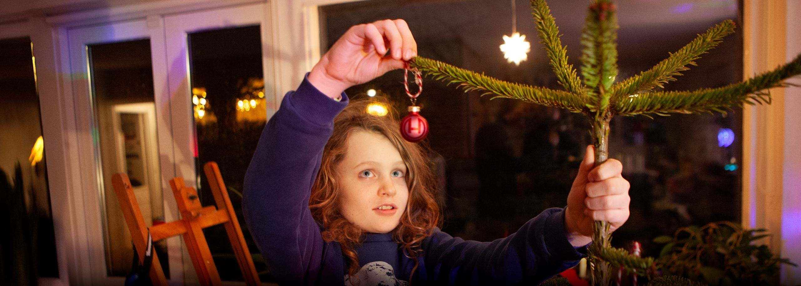 Hindenburg Systems Scandinavian Boy Hanging a Red Christmas Ball with Hindenburg Logo on a Christmas Tree