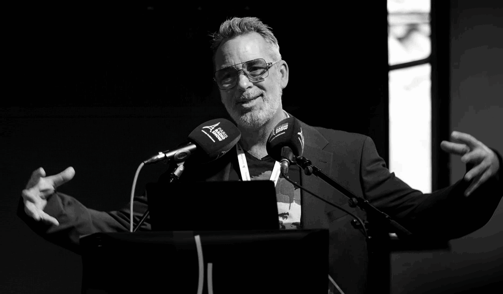 Nick Dunkerley speaking at a keynote event, standing behind microphones and gesturing while presenting
