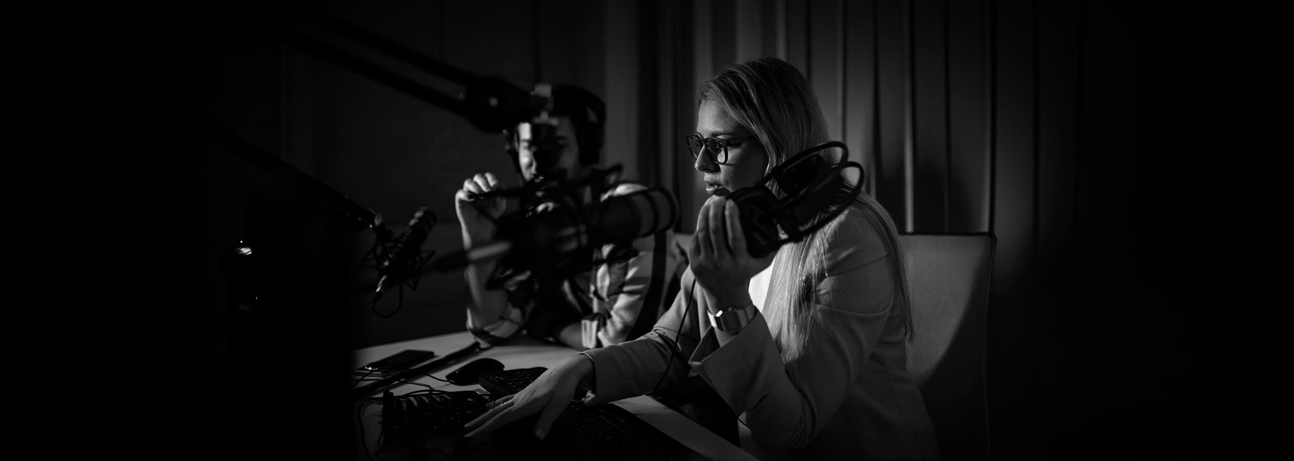 Two journalists working in a radio broadcast studio with microphones and headphones during an audio recording session.