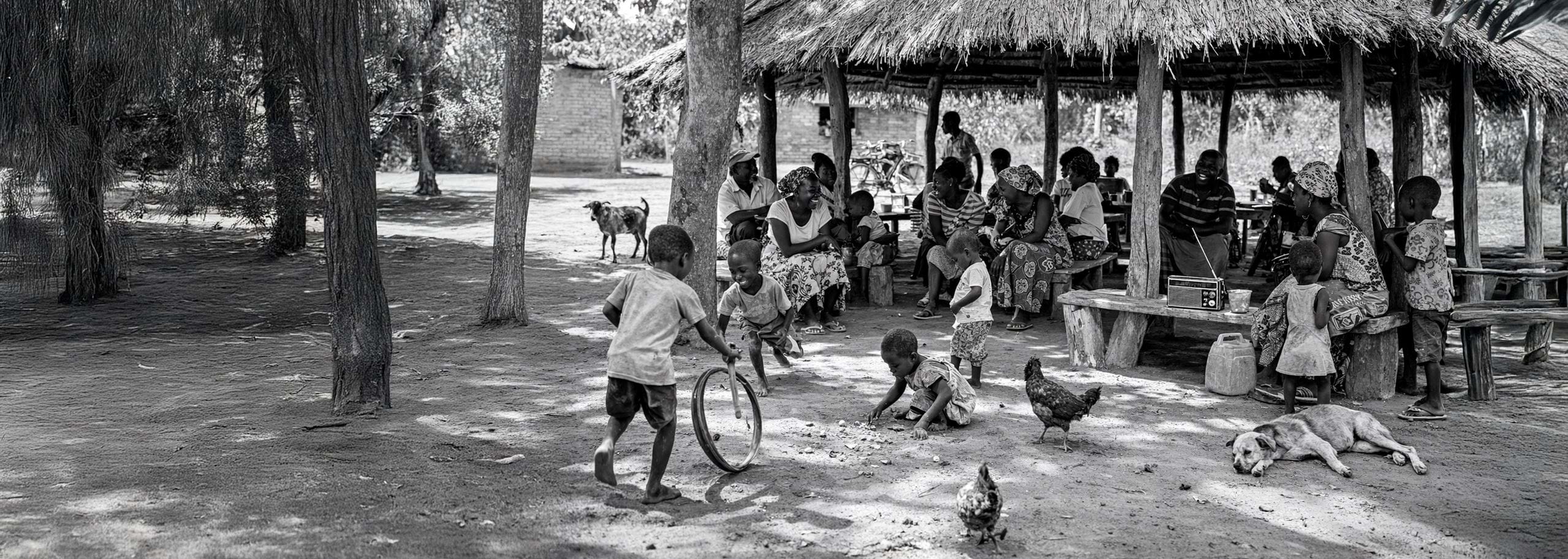 People gathered under a traditional thatched Nsaka shelter while children play nearby and a transistor radio sits on a bench.